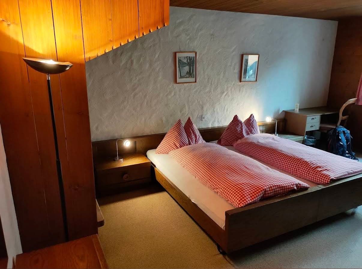 Existing guest room with twin beds, red gingham bedding and warm wood panelling