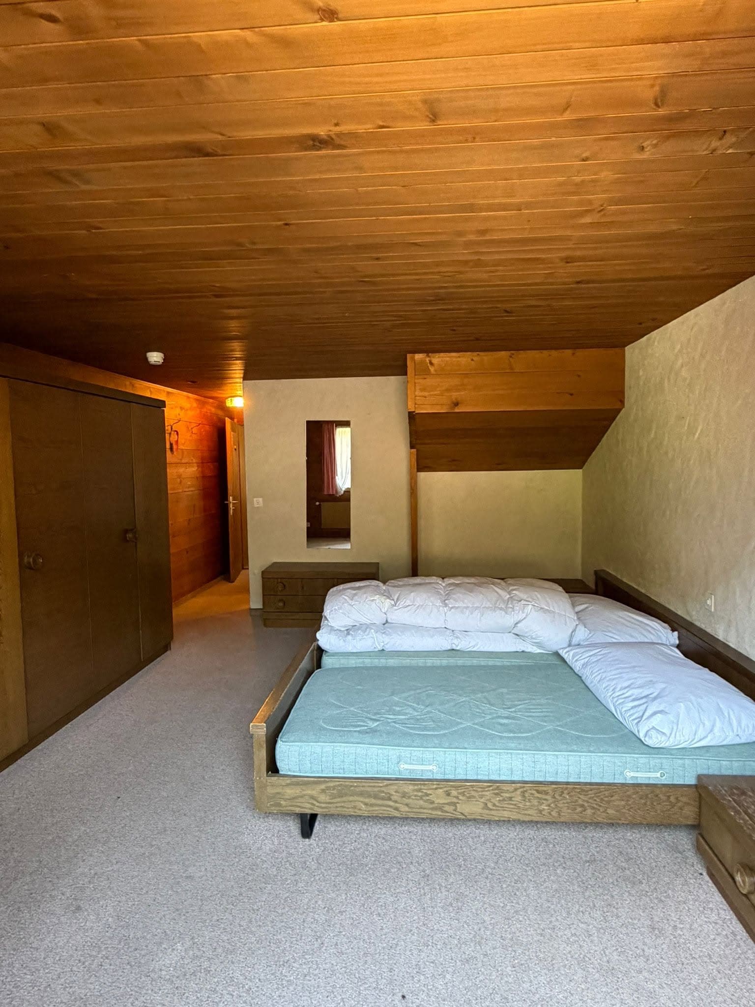 An existing timber-lined guest room with an unmade bed before the planned refresh