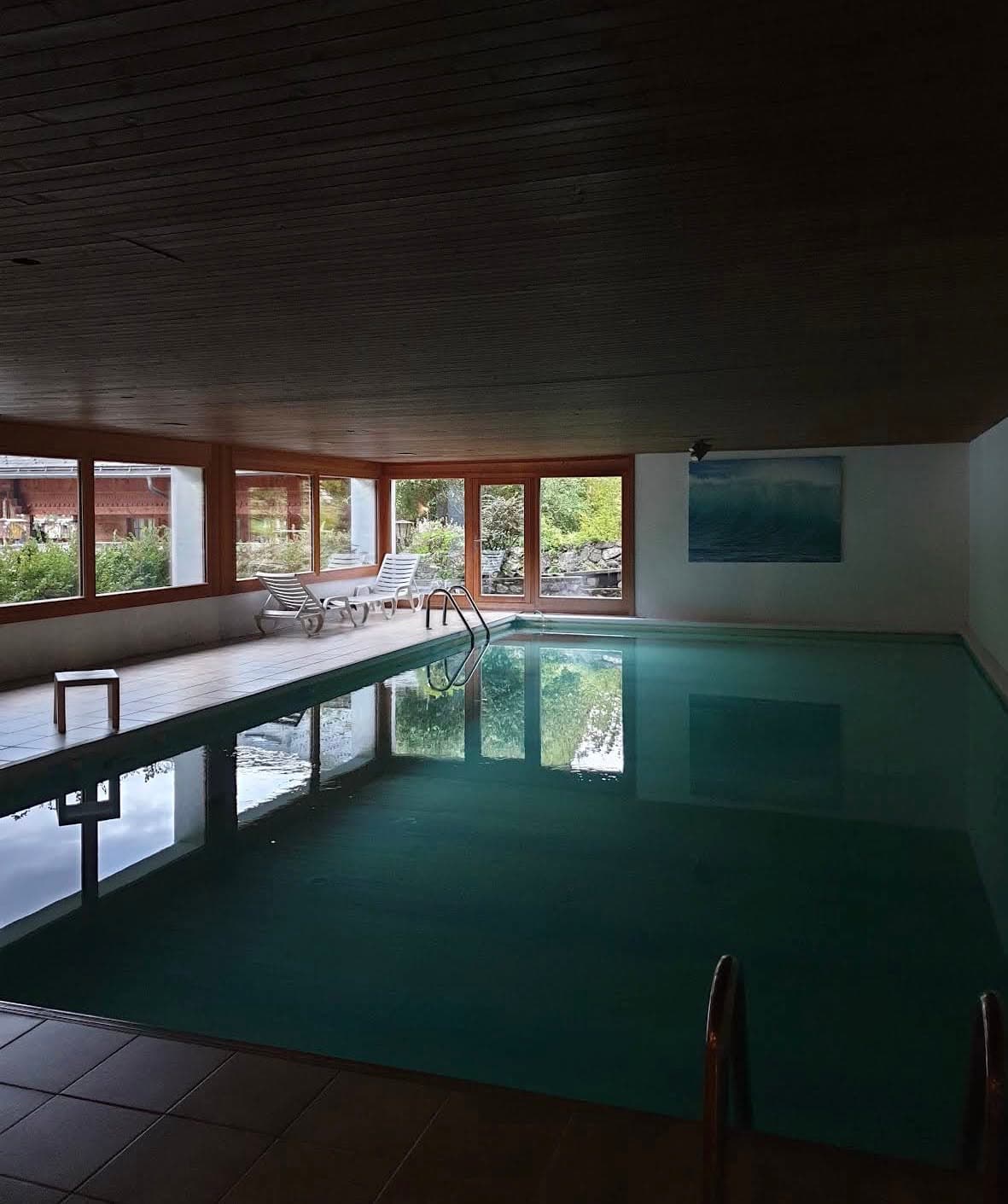 Indoor pool beneath a timber ceiling with windows overlooking the garden